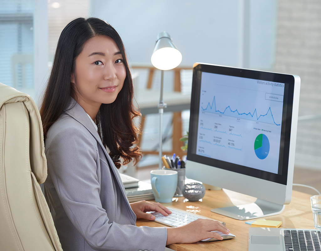 Smiling Asian woman sitting at her office desk and working on a laptop